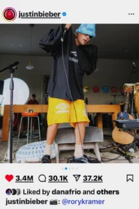 Justin Bieber performing in a studio environment wearing yellow shorts, black shirt, and teal hat